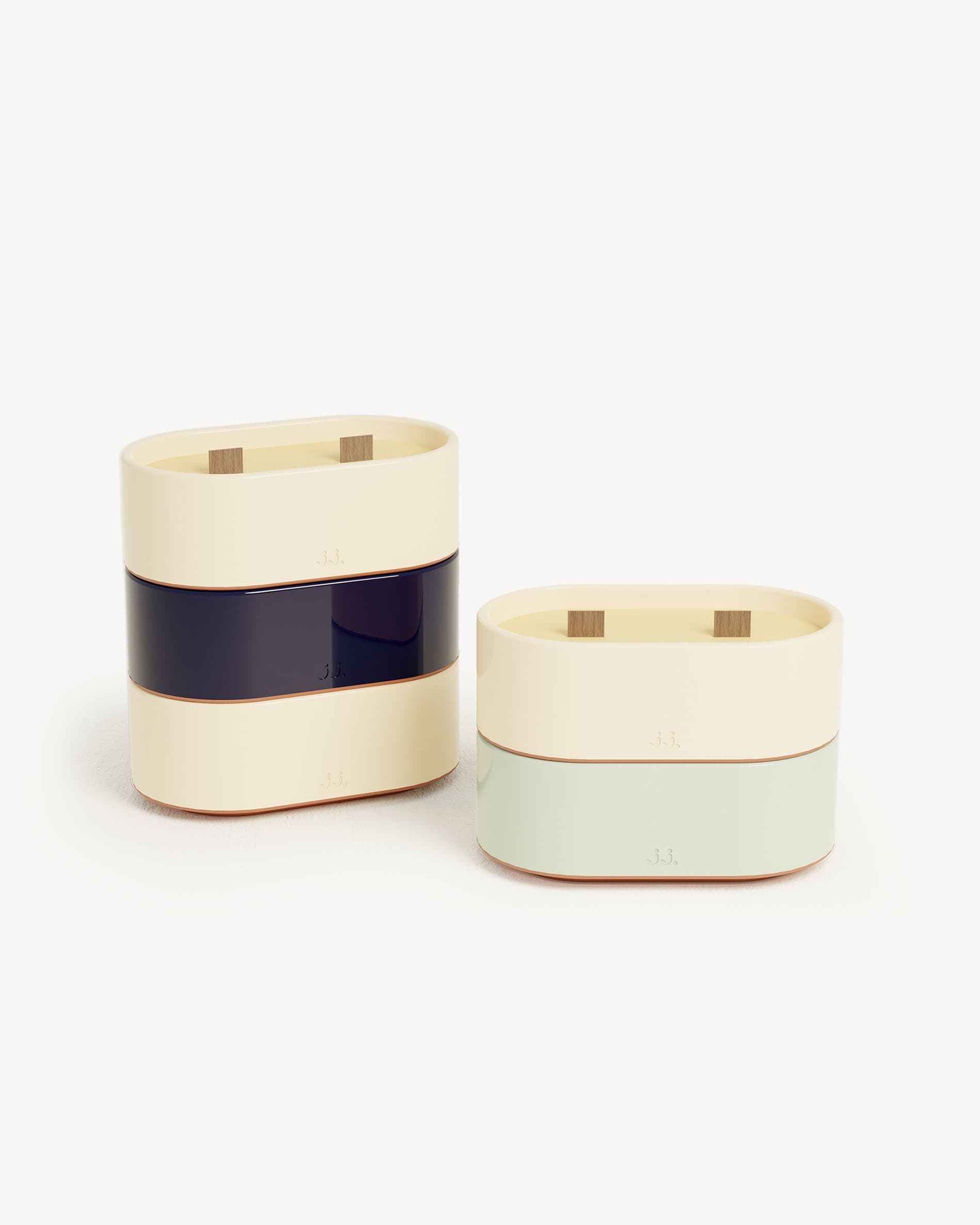 Bougie Totem S en céramique bicolore beige ivoire et bleu marine, parfumée à la citronnelle avec des notes de citron et de sel de mer, présentée aux côtés d’une version vert d’eau à l’eucalyptus.