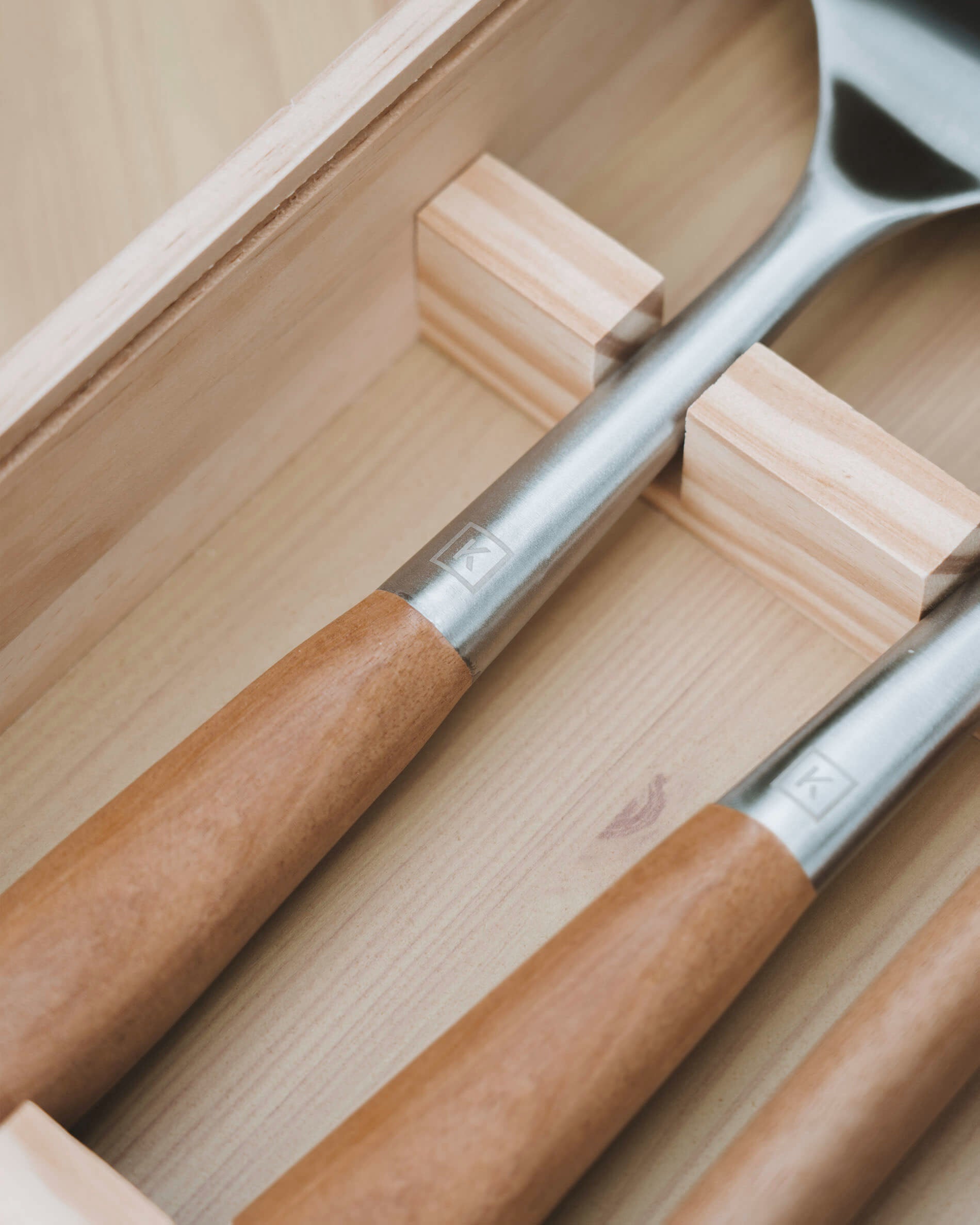 Détail d’ustensiles de cuisine avec manches en bois d’acacia et têtes en acier inoxydable, rangés dans un coffret en bois compartimenté
