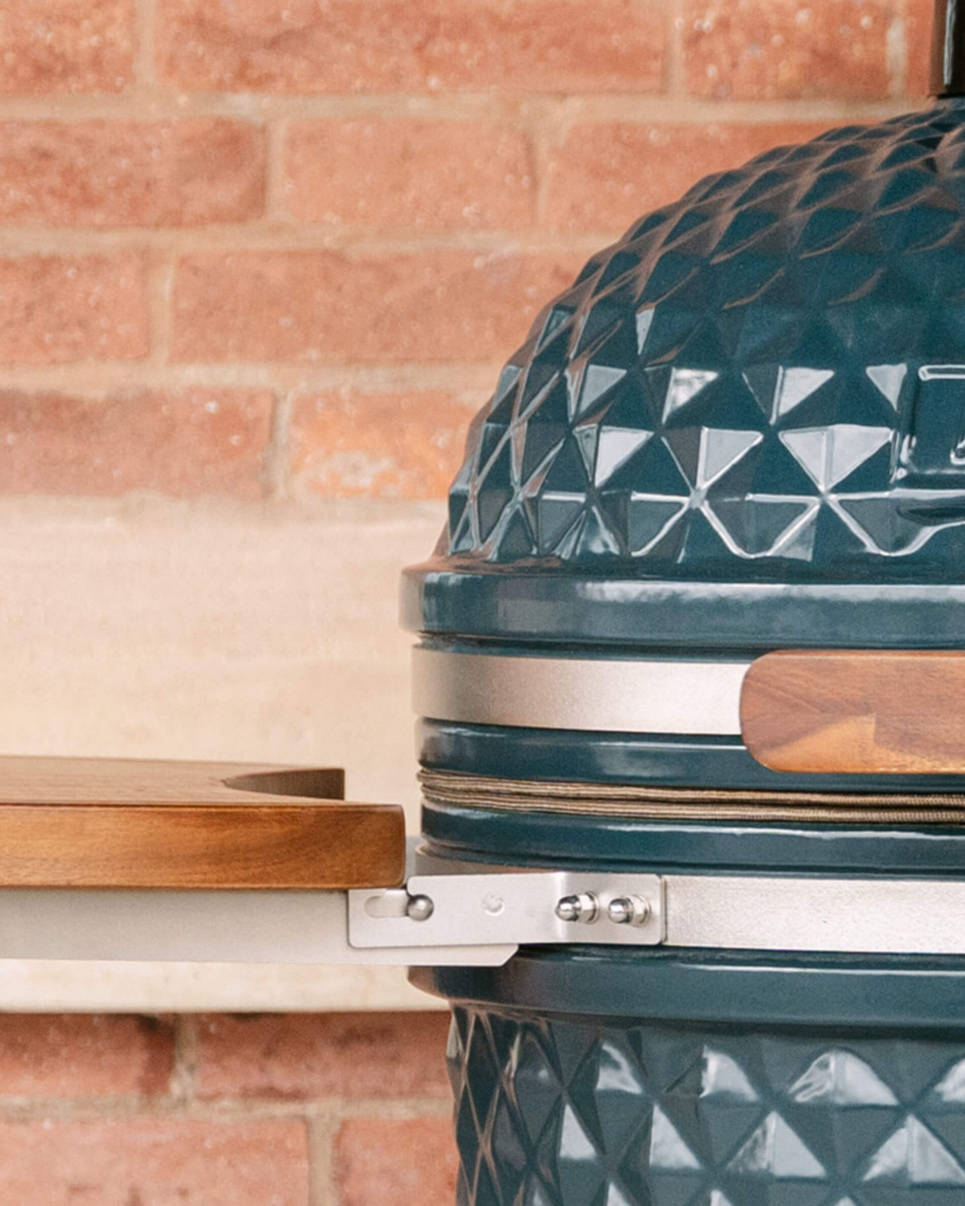 Détail de la fixation latérale d’un plateau en bois sur kamado Kokko, montrant le système de support métallique reliant le plateau au corps en céramique.