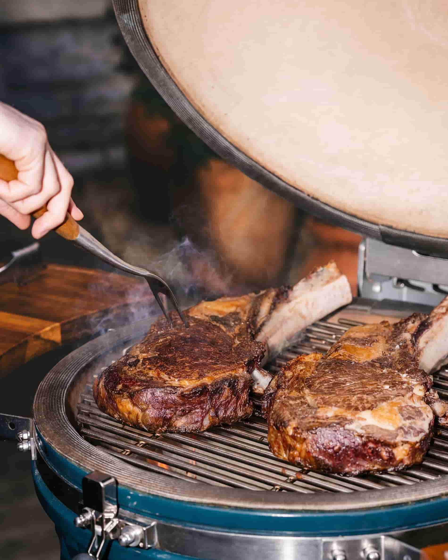 Cuisson de viande sur la grille d’un kamado Kokko XL 22 pouces, couvercle ouvert.