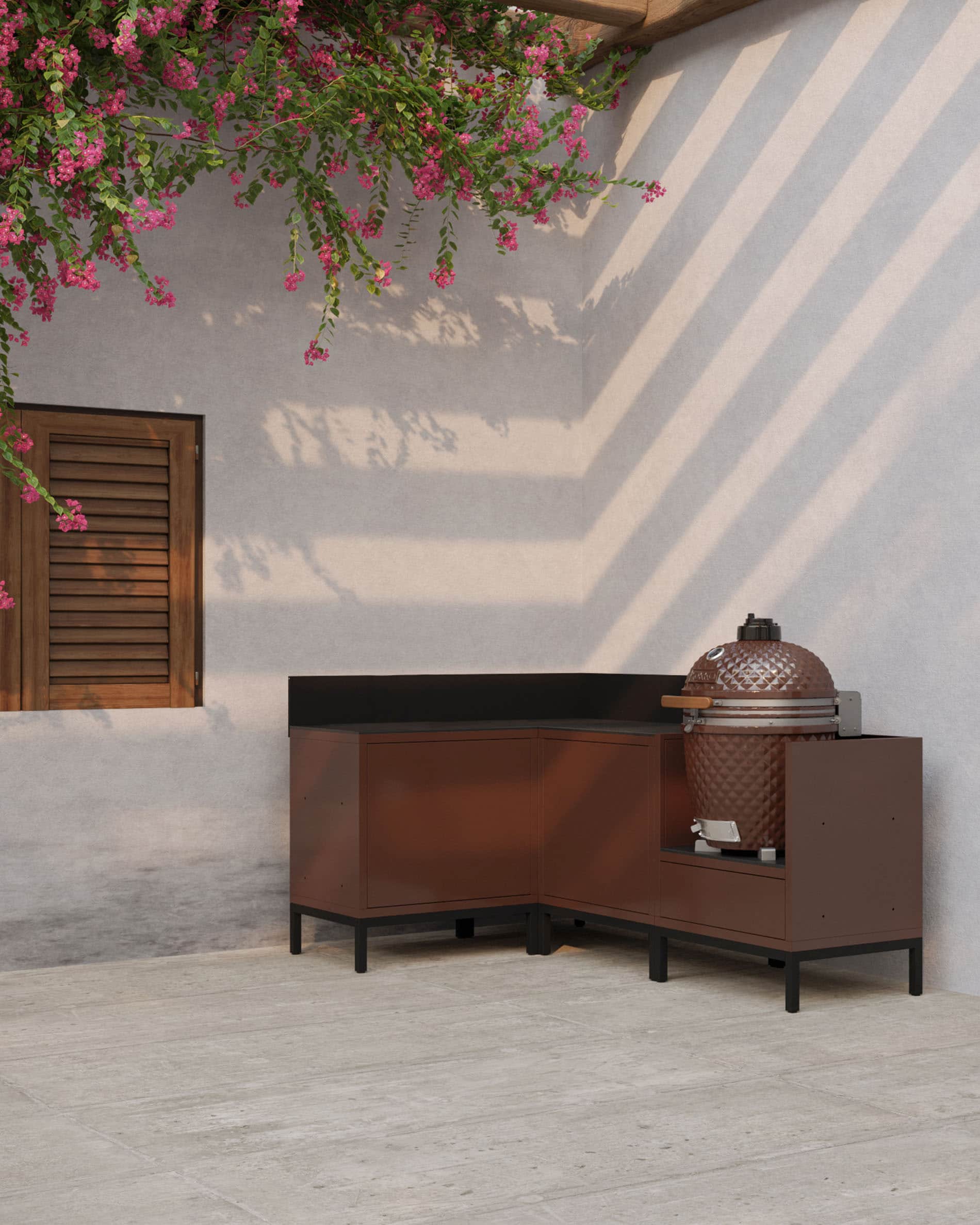 Cuisine pilotis d’angle coloris rouille avec plan de travail sombre, rangements fermés et module dédié à l’intégration d’un kamado en extérieur.