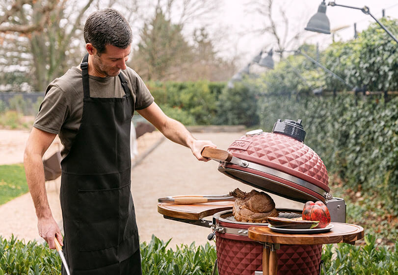 Cuisson d’un rôti dans un kamado Kokko rouge, avec ouverture du couvercle et manipulation des aliments en extérieur.